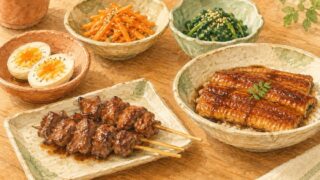 レバーの焼き鳥、うなぎのかば焼き、ゆで卵、にんじんの炒め物、ほうれん草のごま和えが並ぶ食卓の水彩イラスト